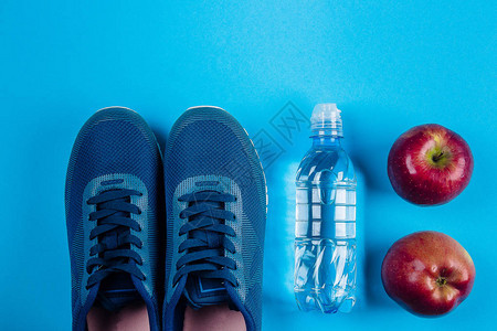 健康生活的概念蓝色运动鞋苹果和水瓶在蓝色背景上的平躺运动器材顶视图片