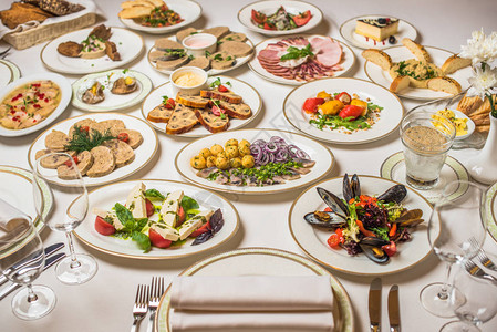 餐桌上有许多不同的菜肴白色桌布上的盘子叉子刀眼镜图片