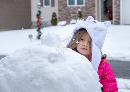 在雪地里玩耍和堆雪人的蹒跚学步的小女孩图片