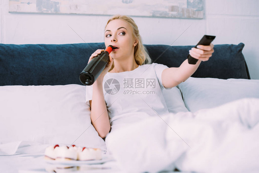 妇女独自在床上庆祝生日时喝酒和看电视图片