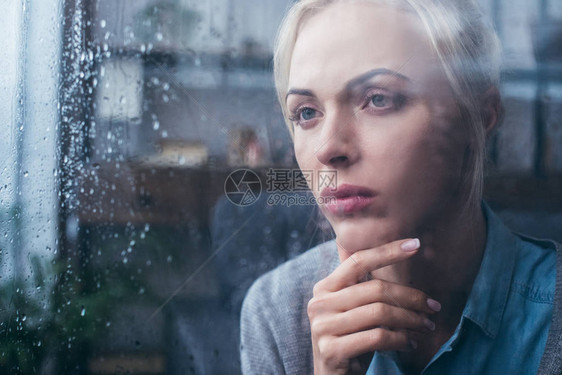 深思痛心的成年妇女用雨滴通过窗口在图片