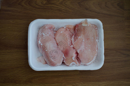 木制背景的白色托盘中的冷冻鸡片生鸡肉图片