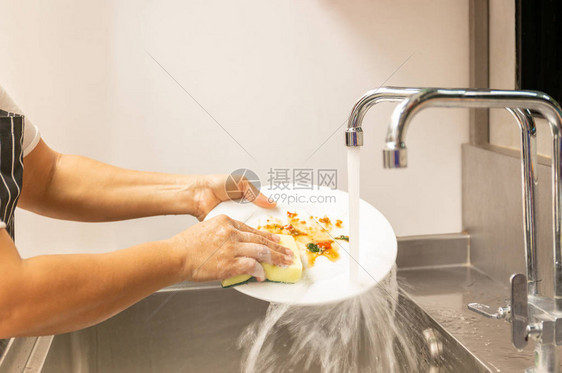 手在厨房水槽里用自来水洗脏盘子图片