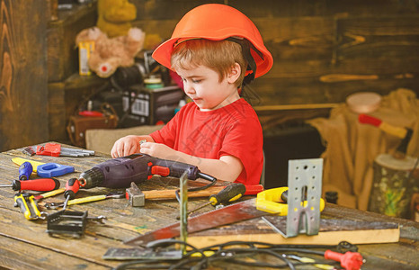小孩玩钻孔和螺栓坐在桌边的戴橙色头盔的侧视男孩工作图片