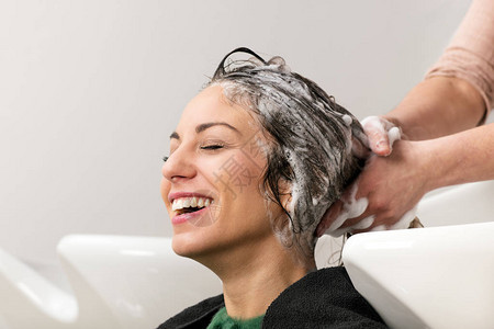 美容院专业发型师在白色陶瓷洗头盆上用洗发水洗头时图片