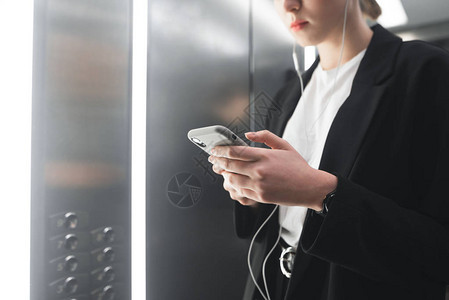 特写一个忙碌的年轻女子在电梯里使用智能手机的照片雄心勃的上班族通过她的手机发短信并在电图片