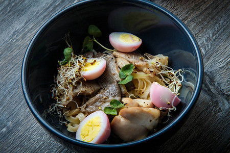 在木桌上的深黑色餐厅碗中供应香菇鸡蛋和小麦芽的顶图片