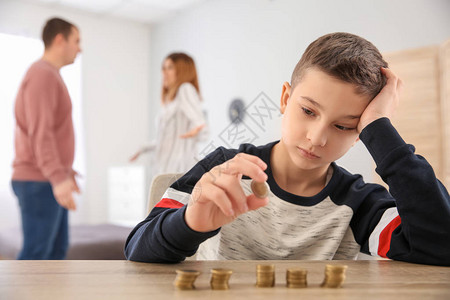 带着硬币和在家争吵的父母的可怜小男孩儿图片