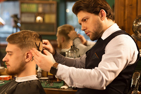 一位英俊的留着胡子的专业理发师在他的理发店工作的侧面照片图片