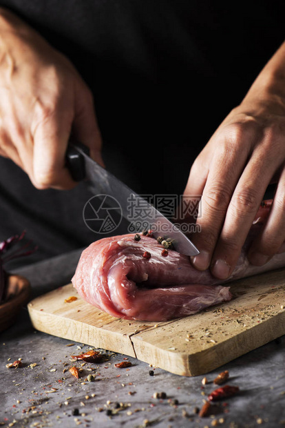 一个白人年轻男子用刀在木砧板上切一块生猪里脊肉的特写图片