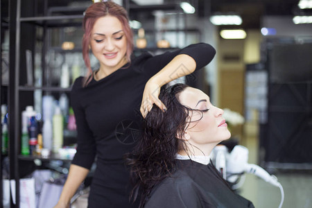 专业发型师在美容工作室为美丽的年轻女子吹干头发专业图片