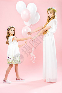 穿着白色优雅礼服的美丽母亲和可爱女儿穿着粉红背景的图片