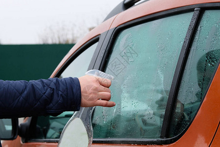 男人用喷雾清洗他的橙色汽车洗汽车窗户背景图片