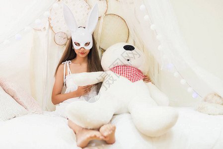 白兔子面罩的黑发美女在贝丁卧室拿着白色大熊娃图片