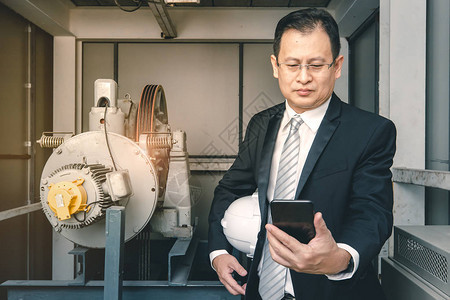 亚洲执行工程师站在工业厂的重型机械旁边图片