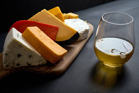 黑光桌面上有不同种类奶酪和白葡萄图片