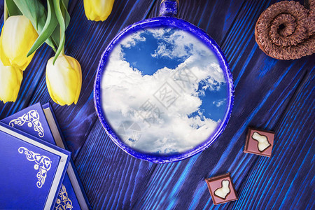 杯内有美丽的天空书籍和蓝色背景上的春天黄色郁金香春天和复活节的概念更图片