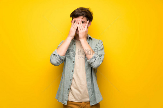在黄色墙壁上的少年用手捂住眼睛用手指看图片