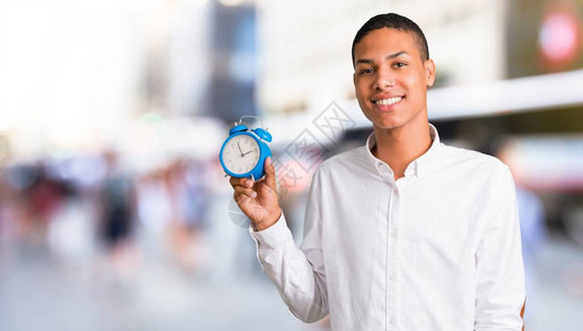 身着白衬衫的非洲青年美国人在市中心拿着古老的闹钟图片