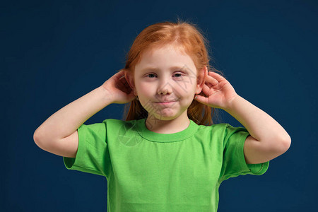 可爱红发小姑娘的肖像试图听到有人把她的手放在耳朵上蓝色背图片