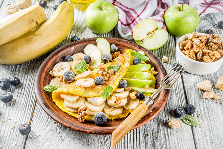 健康早餐食品带水果浆果和坚果的甜馅鸡蛋煎卷质朴的木质背景复图片