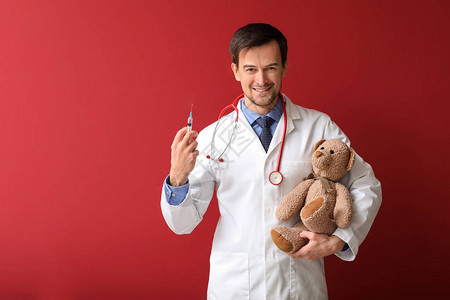 彩色背景上带玩具熊和注射器的儿科医生图片