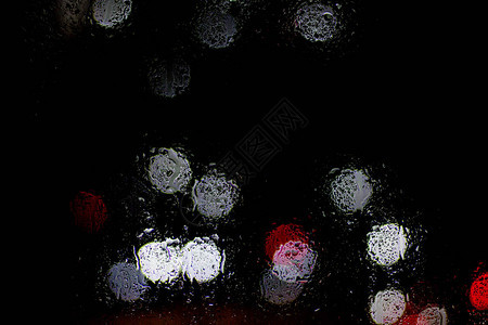 Bokeh夜间城市灯光在雨中湿玻璃后面图片