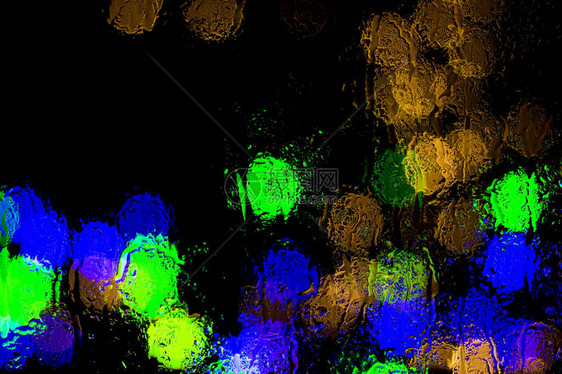 Bokeh夜间城市灯光在雨中湿玻璃后面图片