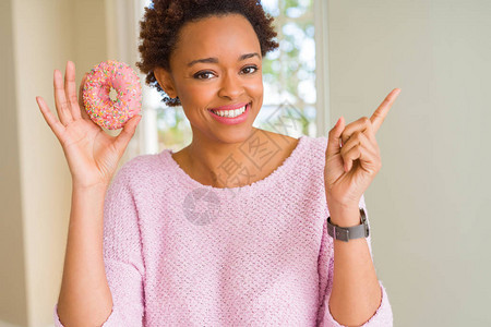 年轻的非裔美国女人吃粉红糖甜圈非常快乐用手和指图片