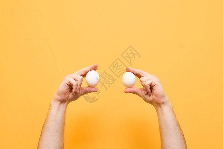 男人的手拿着黄色背景上的两个白鸡蛋带鸡蛋的手被隔离在黄色背景上背图片