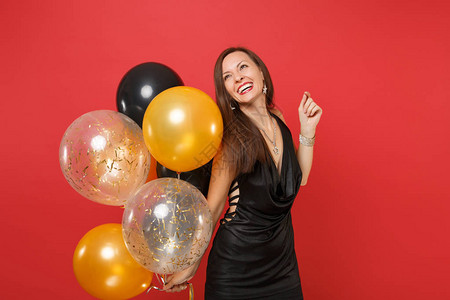微笑的小女孩穿着黑色小礼服庆祝抬头拿着气球孤立在鲜红色的背景图片