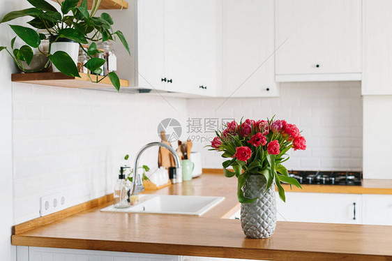 花瓶里的郁金香花束站在厨房的木制台面上斯堪的纳维亚风格的现代白色u形厨房厨房里的架子上放图片