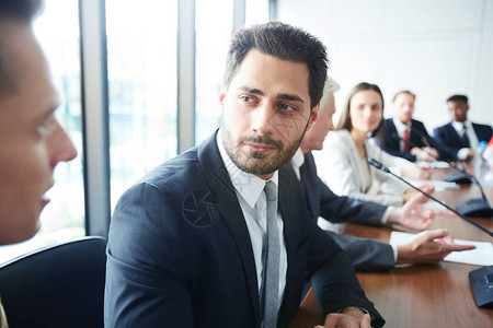 英俊商人坐在会议室会议桌旁看着同事的头肩肖图片