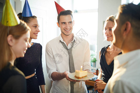 戴着生日帽子的快乐男人给他的一个朋友盘子一块蛋糕图片