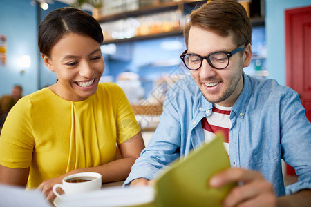 快乐的年轻同事在休息时看书同时在咖啡馆图片