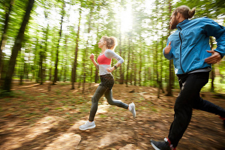 年轻活跃男子和他的女友在阳光明媚的一天在森林里慢跑在图片