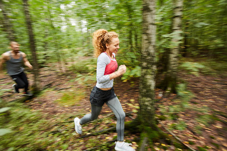 年轻活跃的女和她的男朋友早上在模糊的绿树丛中奔跑图片