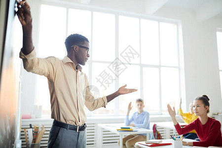 自信的非洲美国年轻老师指着黑板与中学生上课时说话图片