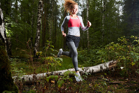 快乐的年轻女运动员在清晨沿着森林路行走时跑过B图片
