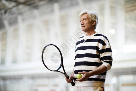 有球拍和球的活跃高级网球运动员站在体图片