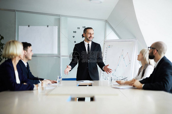 自信的商务教练站在员工面前的桌子旁图片