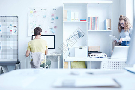 一位年轻的分析家或设计师坐在电脑屏幕前的办公桌旁图片