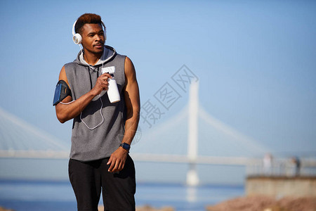 穿戴智能手机臂带的耳机在海岸线上行走和饮用水边考虑自然问题时图片