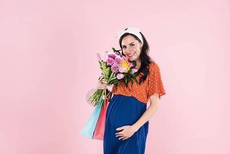 持有购物袋和鲜花的浪漫孕妇在粉图片