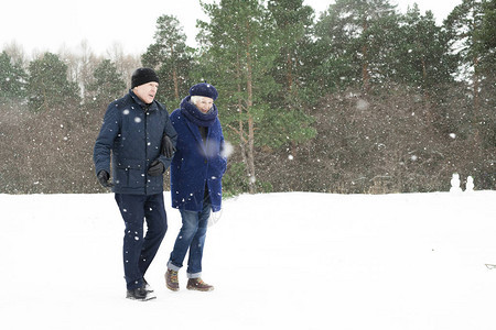 现代老年夫妇在冬季森林中行走的全长肖像图片