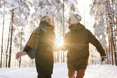 玩耍情侣的肖像在冬季森林中向镜头跑来微笑着快乐图片
