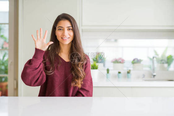 年轻漂亮的女人在家里展示并用五号手指向上指着图片