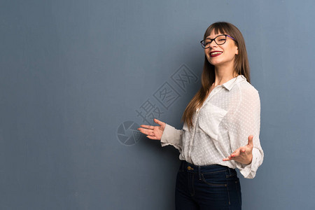 在蓝墙上戴眼镜的女人骄傲而满足于爱自己的概图片