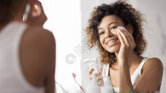 洗手间镜子前用棉垫擦脸的美国年轻女子在卫生间用棉图片