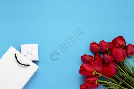 白色礼品袋一个小白色礼品盒和蓝色背景上的一束红色郁金香概念提供订婚图片